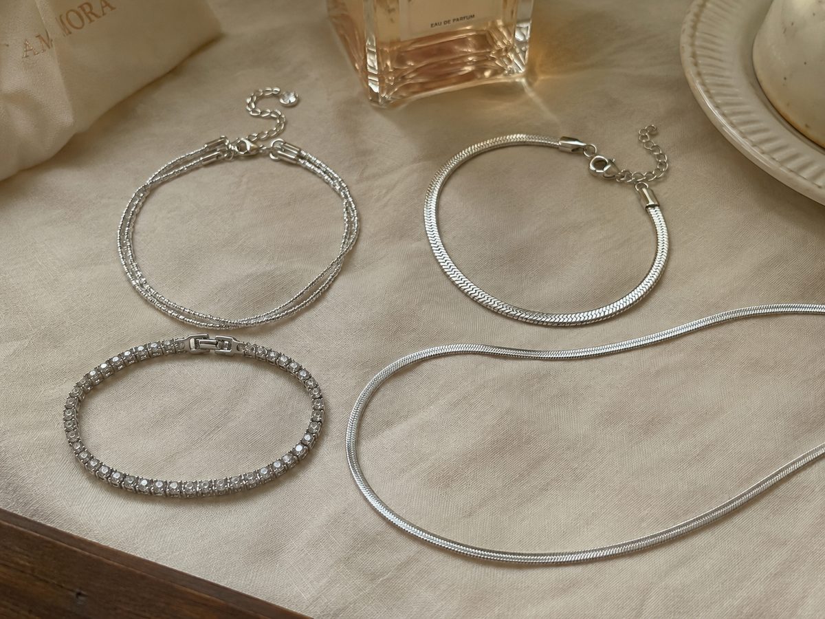 A flat-lay of Amora hero pieces — ankle chain, snake bracelet, tennis bracelet and a necklace